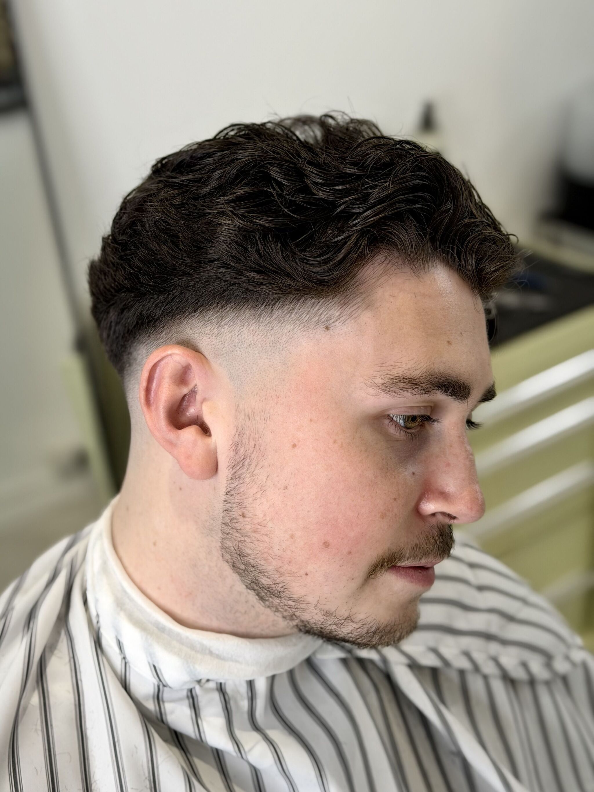 Curly top with a taper fade and shaped beard